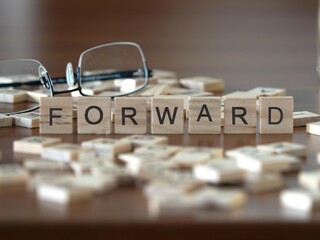 forward word or concept represented by wooden letter tiles on a wooden table with glasses and a book
