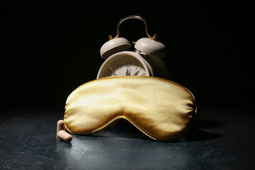 Sleep mask, alarm clock and earplugs on dark background