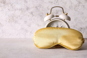 Stylish sleep mask and alarm clock on light background