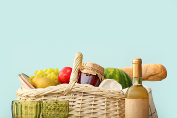 Wicker basket with tasty food and wine on color background