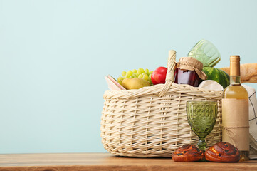 Wicker basket with tasty food and wine for picnic on table against color background