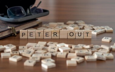 peter out word or concept represented by wooden letter tiles on a wooden table with glasses and a...