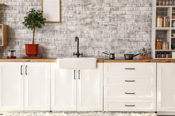 Interior of modern kitchen with white counters and brick wall