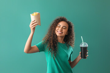 Young African-American woman with french fries and cola on green background