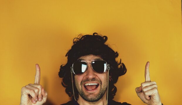 Happy hispanic funny young bearded man pointing with both fingers hands gesture at copy space advertising new promotion, presenting sale offer standing isolated on yellow background.