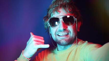 Photo of stylish young man isolated on neon color background wearing sunglasses while making cool sign. Studio shot.