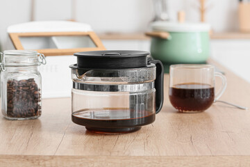 Coffee machine pot with hot beverage on wooden counter in kitchen, closeup