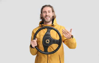 Handsome man with steering wheel on grey background