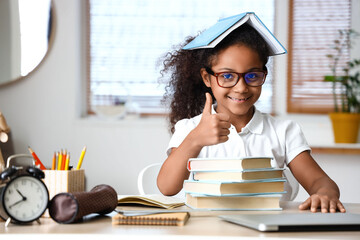 Little African-American girl with books showing thumb-up at home