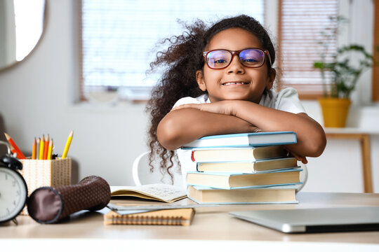 Little African-American girl with books studying at home