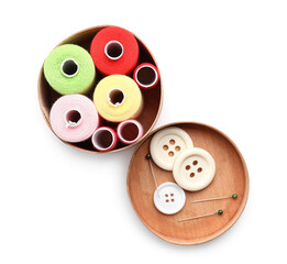 Wooden box with sewing thread spools, buttons and pins on white background