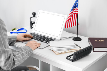 Woman using laptop on table with USA flag near light wall