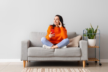 Beautiful young woman with mobile phone resting on couch at home