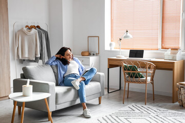 Beautiful woman with book resting on couch at home