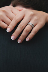 Close up of an asian woman's hands draped around the neck of a man in a suit