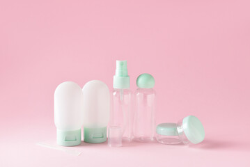 Set of empty travel cosmetic bottles and jars on pink background