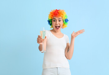 Funny young woman in colorful wig and with champagne on blue background. April fools' day celebration