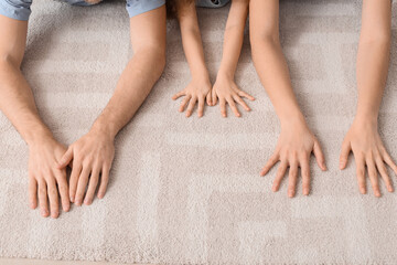 Hands of young family lying on soft carpet at home