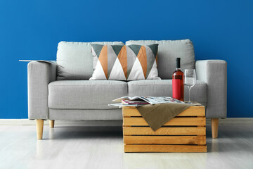 Glass and bottle of wine on table and stylish sofa near blue wall