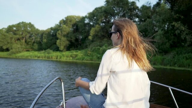 Beautiful woman sitting on front deck of the wooden vintage speedboat sailing in jungle river. It is warm and sunny summer evening with light wind.