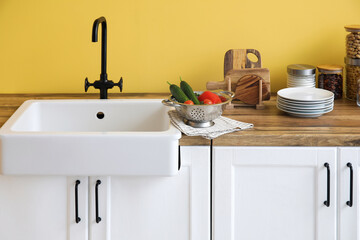 Fototapeta na wymiar Counters with sink, food and kitchen utensils near yellow wall