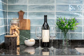Bottle of red wine with crystal glasses on black marble countertop in a blue tiled kitchen