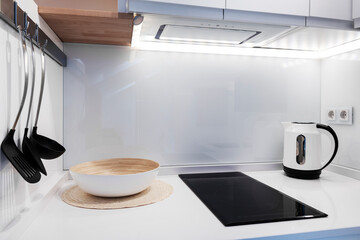 Kitchen with a small white worktop with a two-burner ceramic hob, a white water heater and black kitchen utensils