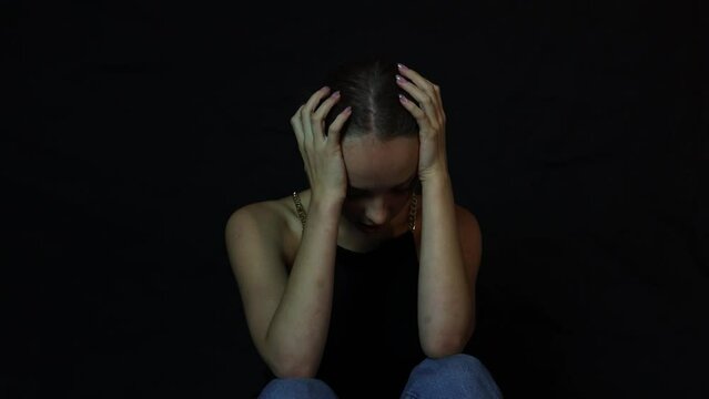 Young sad teenage girl sitting in front of a black background