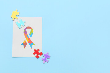 Paper sheet with awareness ribbon and puzzle pieces on blue background