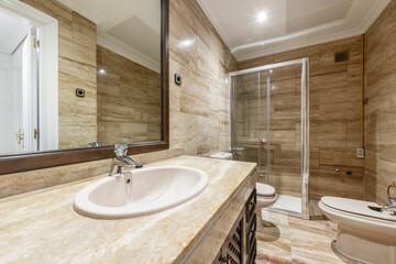 One-piece bathroom with white porcelain sink with mesh doors on cream marble under rectangular mirror with brown frame and walk-in shower