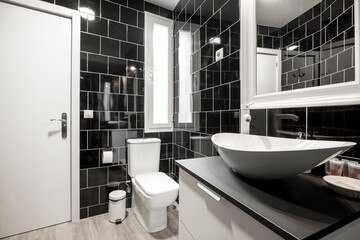 Fototapeta na wymiar Bathroom with black tile walls, white framed mirror on the wall and tall wooden sink cabinet, ceramic tile flooring and white wooden door