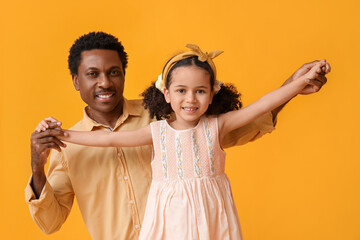 Portrait of little African-American girl and her father on yellow background