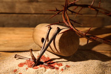 Crown of thorns with nails, mallet, blood drops and sand on wooden background