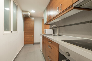 kitchen with wooden furniture with gray wooden countertop with white washing machine and matching microwave, black ceramic hob gray ceramic floors