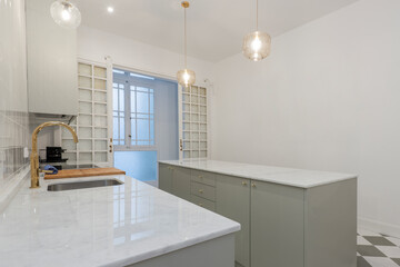 Kitchen with long white marble countertops with sink and glazed wooden doors and several lamps on the ceiling