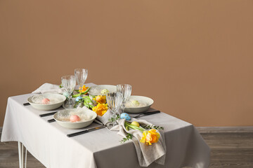 Stylish setting with floral decor and Easter eggs on table near color wall