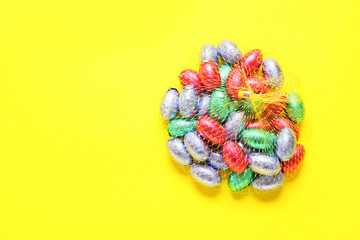 Mesh bag with chocolate Easter eggs on yellow background