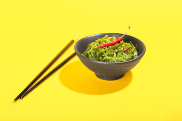 Bowl with healthy seaweed salad on yellow background