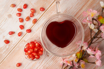Fresh Pomegranate Juice served in a heart-shaped glass with fresh pomegranate fruits on wooden table. Vitamins and minerals. Healthy drink concept.