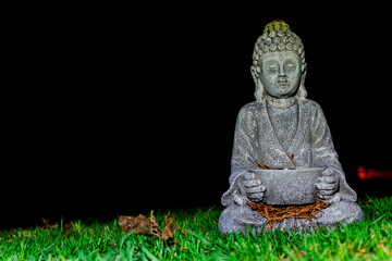 Radiant green grass in front of pitch-black background with Buddhist statue sitting on top.