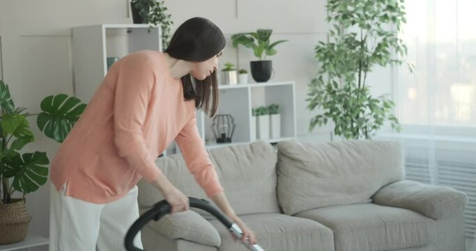 Pregnant woman suffering with backache while cleaning carpet with a vacuum cleaner at home