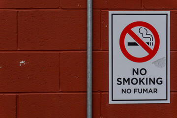 Red painted cement wall with no smoking sign in foreground. Gray metal pipe leading upward.