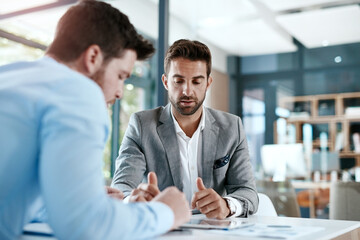 Digitizing a financial discussion. Cropped shot of two young businessmen using a digital tablet while going through paperwork together in a modern office.