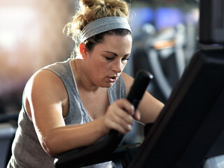 Push yourself and keep it going. Shot of a determined looking woman working out on an elliptical machine in the gym. - obrazy, fototapety, plakaty