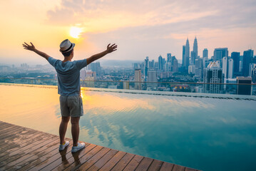 Obraz premium Travel man happy and raise hand up freedom enjoy view of beautiful landscape of Kuala Lumpur skyscraper in morning, Kuala Lumpur city, Malaysia.