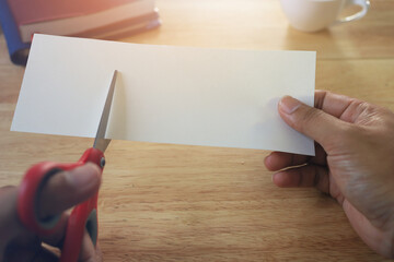 Obraz premium Holding scissors and cutting blank white paper on a wooden work table.