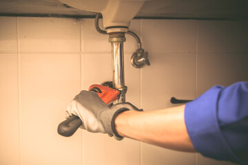 Technician plumber using a wrench to repair a water pipe under the sink. Concept of maintenance,...