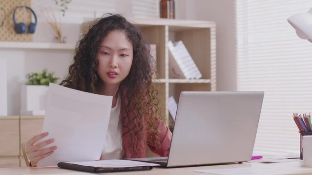 At home, an Asian designer works on a desk with a laptop, searching for jobs and paperwork.Designer web development website template design user ui application on paper.