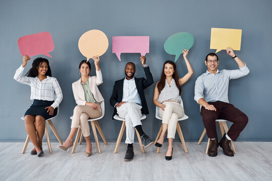 Its A Hot Topic In The Business World Right Now. Portrait Of A Group Of Businesspeople Holding Speech Bubbles While Sitting In Line Against A Grey Background.