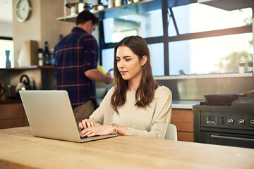 The best is browsing in the comfort of your home. Cropped shot of a young woman working on a laptop with her boyfriend in the background at home.